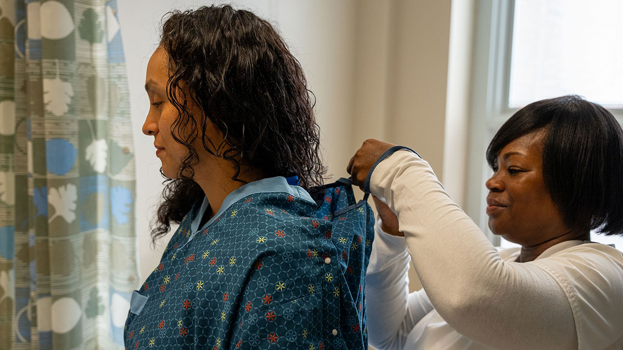 Nurse assisting patient with surgical gown